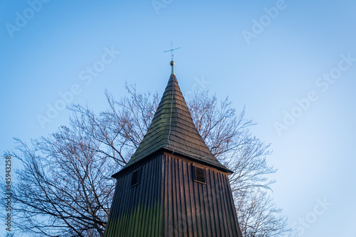 Obraz na płótnie Metal cross on the peak of the belfry of the church of St. Michael the Archangel in Katowice, Silesia, Poland. Wooden temple from the beginning of XVI century. Leafless tree in the background. w salonie