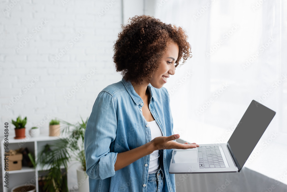 side view of smiling african american woman with curly hair holding laptop while working from home. side view of smiling african american woman with curly hair holding laptop while working from home.