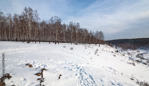Winter landscape with birches and sky from the high rocky river bank