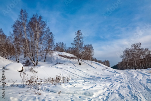 Winter landscape with birch trees on the mountain bank of the river, snow and blue sky with clouds © Александр Коликов