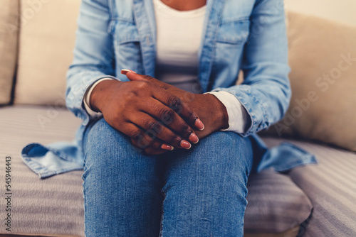 Closeup shot of a woman sitting on couch with her hands clasped at home during the day.