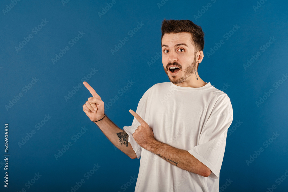 Portrait of casual young man wearing casual clothes posing isolated over blue background smiling and looking at the camera pointing with two hands and fingers to the side. Portrait of casual young man wearing casual clothes posing isolated over blue background smiling and looking at the camera pointing with two hands and fingers to the side.