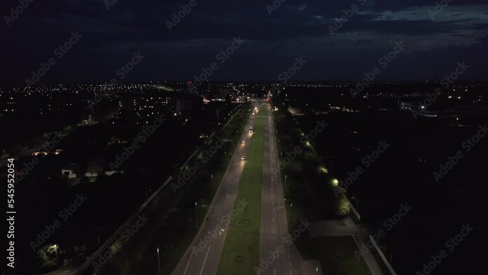 Aerial view of cars on the road near the recreation area and night city panorama with flashing lights. Zoom out Aerial view of cars on the road near the recreation area and night city panorama with flashing lights. Zoom out