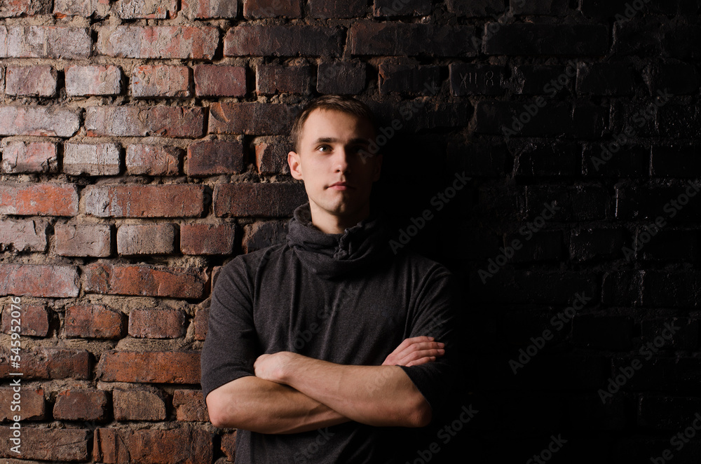 young man in a black jacket against the background of a brown, red and black brick wall young man in a black jacket against the background of a brown, red and black brick wall