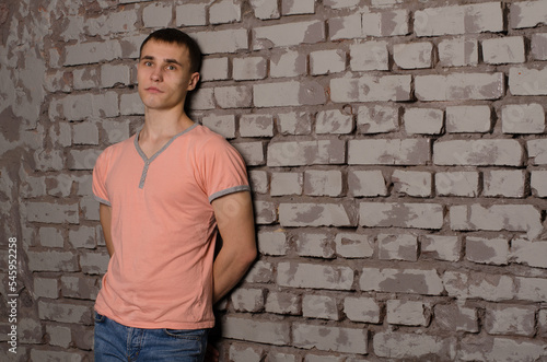 young man in a pink t-shirt standing against a gray brick wall, space for text