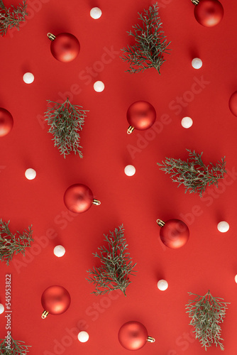 Christmas pattern with red baubles, evergreen branches and white balls on red background. Minimal New Year concept.