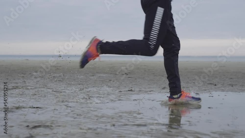 Slow motion close-up video of men's legs running through mud and puddles. Training in difficult conditions, morning run after rain in nature. High quality 4k footage