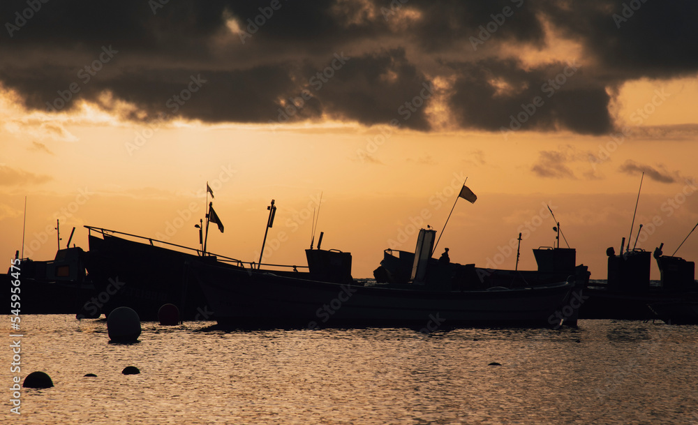 Fototapeta premium Silhouette many fishing ships in harbor on seaside with altostratus clouds in colorful sunrise sky background and reflection on sea surface at morning time