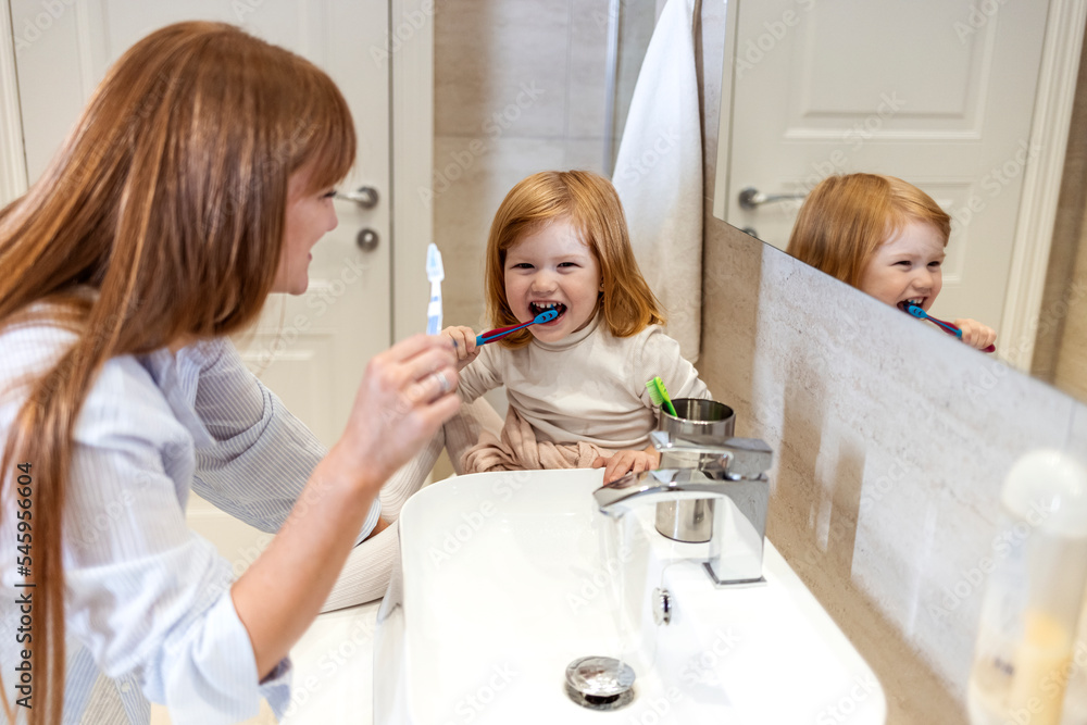 Shot of a mother and her little daughter brushing their teeth in the bathroom. Photo of a cute little girl and her mother teaching her how to brush teeth in the bathroom of their apartment; Shot of a mother and her little daughter brushing their teeth in the bathroom. Photo of a cute little girl and her mother teaching her how to brush teeth in the bathroom of their apartment;