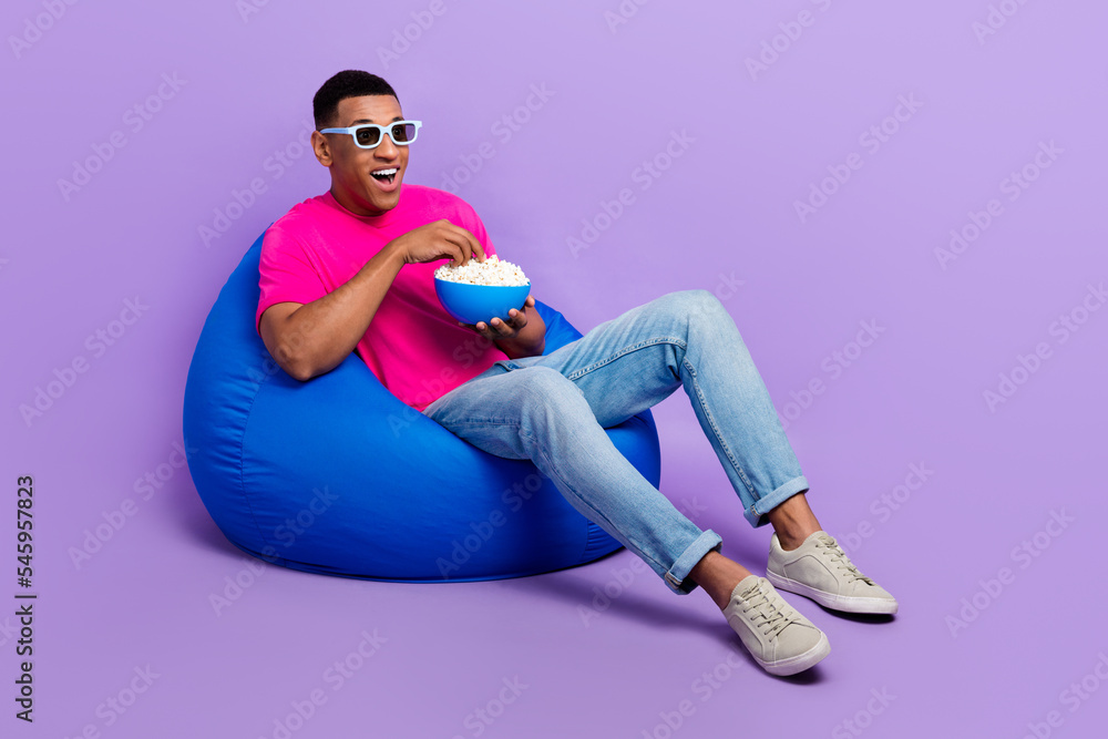 Full body photo of crazy astonished person sit cozy bag hold popcorn plate isolated on violet color background Full body photo of crazy astonished person sit cozy bag hold popcorn plate isolated on violet color background