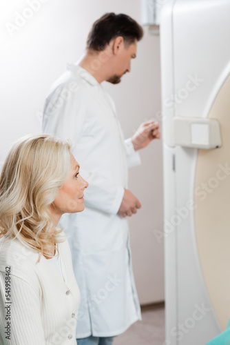 blonde middle aged woman near radiologist and computed tomography scanner on blurred foreground.