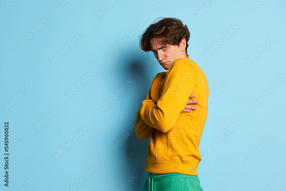Portrait of young man with curly hair posing with offended funny face isolated over blue background