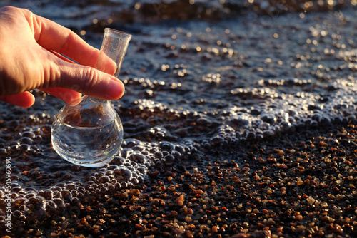 Hand holding water sample for analiysis from the sea, sunlight. Ecology concept