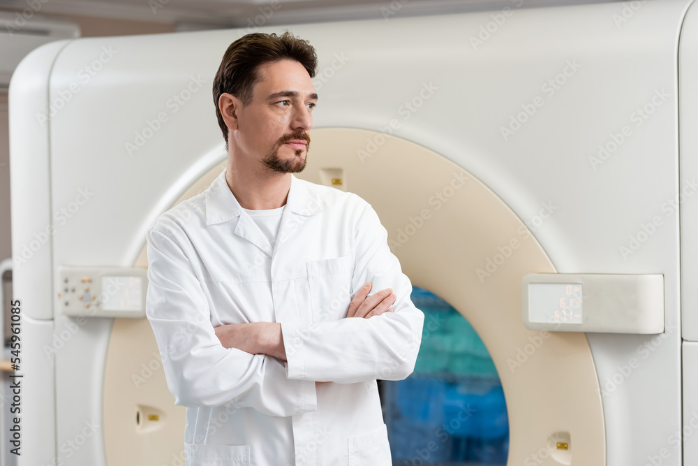 serious bearded radiologist standing near ct scanner in clinic and looking away. serious bearded radiologist standing near ct scanner in clinic and looking away.