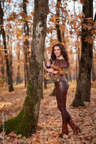 Portrait of a beautiful woman in the forest on a sunny autumn day with a glass of red wine