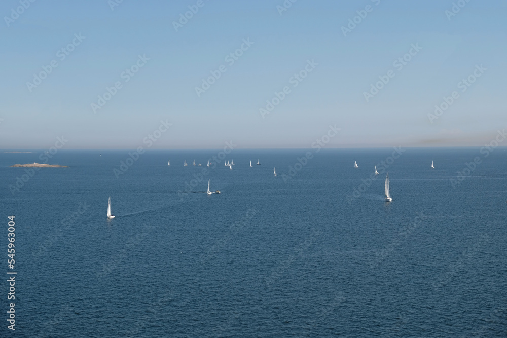 Aerial view of sailboats against blue water with waves and ripples. Many yachts with white sails are sailing. Perfect content for posters or advertising banners, creative projects.