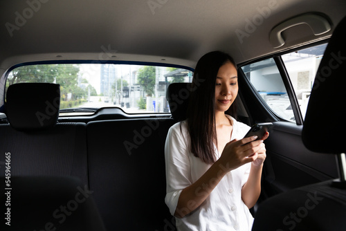 Young asian woman sitting in the backseat of a car using her cell phone to communicate in the city during the day © comzeal