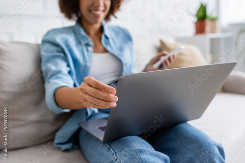 cropped view of african american woman using laptop while sitting on couch.
