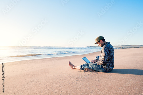 mature latin man sitting on the beach sand with his notebook working at sunset © oscargutzo