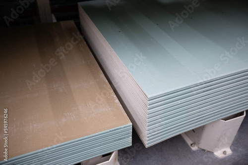Sheets of moisture-resistant drywall of different brands are stacked in bundles