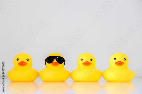 Four yellow rubber ducks in a row, one standing out wearing black sunglasses, organisation concept, get one’s ducks in a row. Copy space.