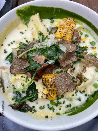 Closeup shot of a spinach broth with corn, pasta, and grated truffles served on a white plate