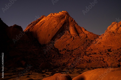Breathtaking view of a red rocky mountain in a desert  illuminated by sunset sunlight in Namibia
