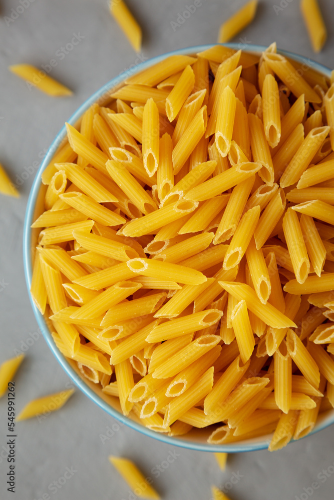 Homemade Raw Dry Mini Penne Pasta in a Bowl on a gray background, top view. Flat lay, overhead, from above. Close-up. Homemade Raw Dry Mini Penne Pasta in a Bowl on a gray background, top view. Flat lay, overhead, from above. Close-up.