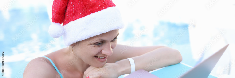 Woman in red santa claus hat looking at laptop on sunbed Woman in red santa claus hat looking at laptop on sunbed
