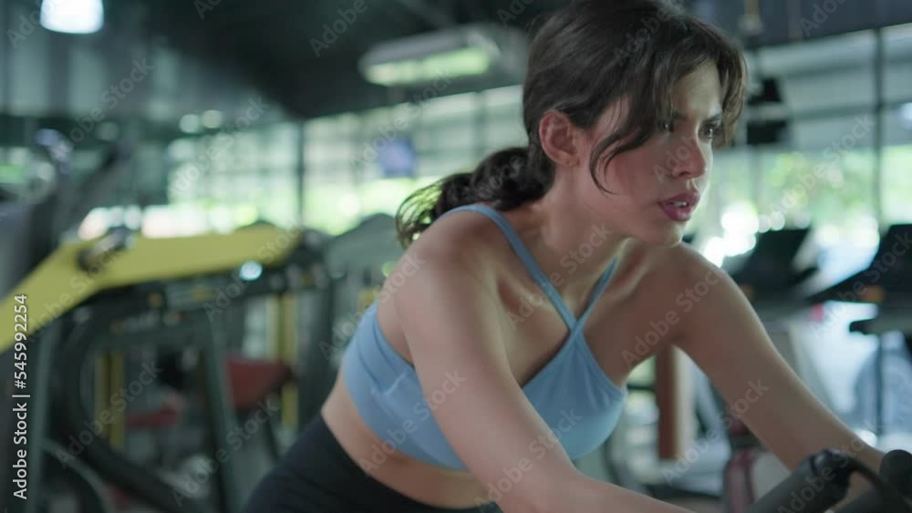 Attractive, young beautiful woman athlete workout on exercise with concentration in gym. Fitness female using equipment bike spinning motion cardio training indoor. Healthy lifestyle concept. Attractive, young beautiful woman athlete workout on exercise with concentration in gym. Fitness female using equipment bike spinning motion cardio training indoor. Healthy lifestyle concept.