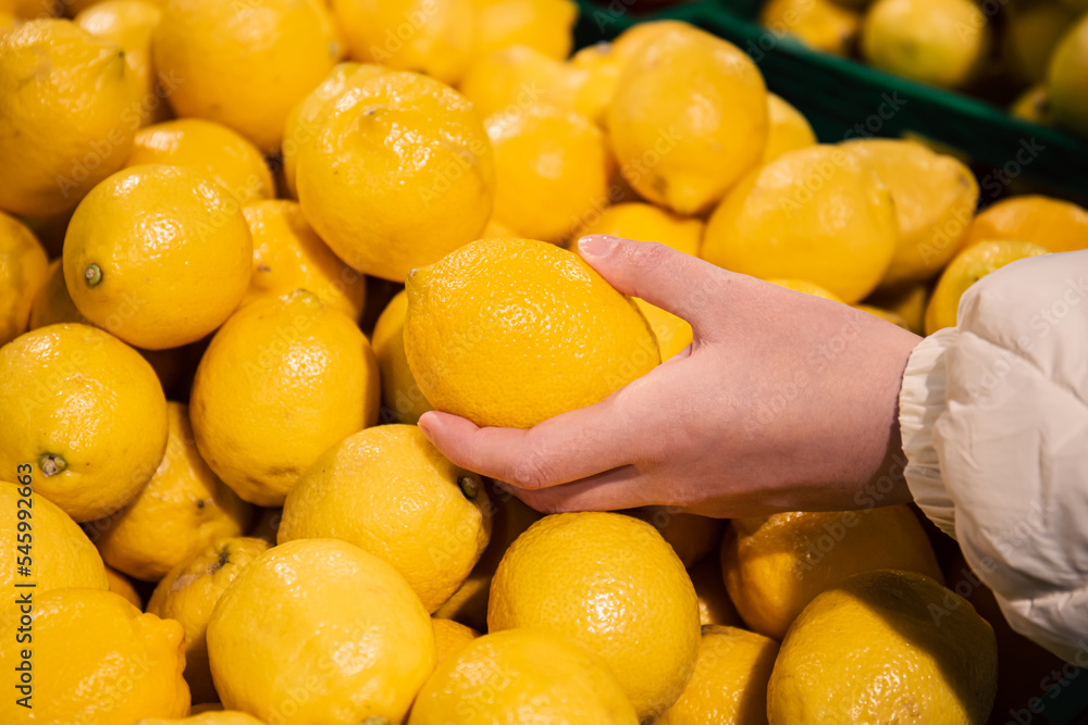 A woman chooses lemons in a supermarket, close-up.