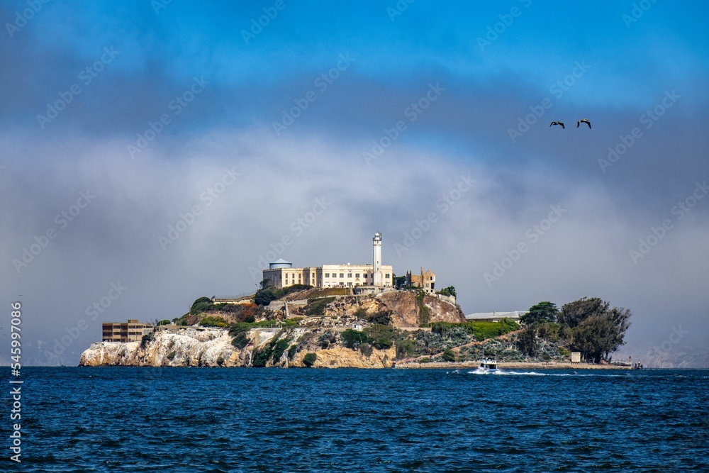 Architecture and a lighthouse on the top of a rocky cliff in the blue water under cloudy sky