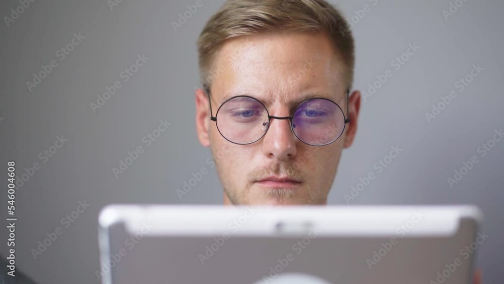 A man with glasses is watching a tablet at home. A man with glasses is watching a tablet at home.