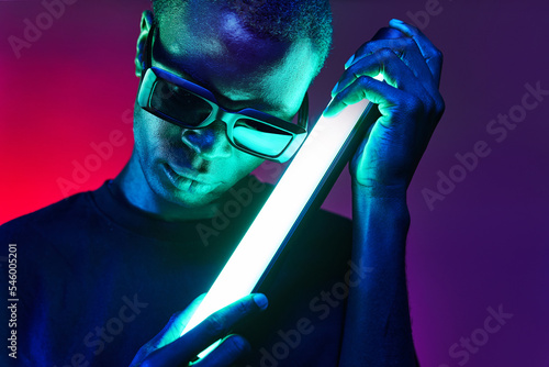 Extravagant black man in sunglasses with fluorescent lamp in hands