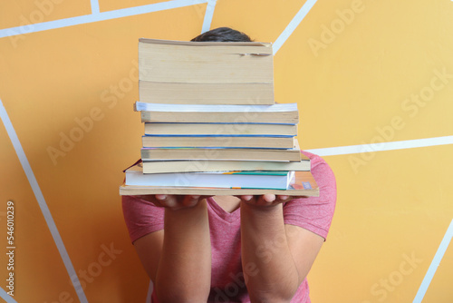 boy holding stacked books - yellow wall