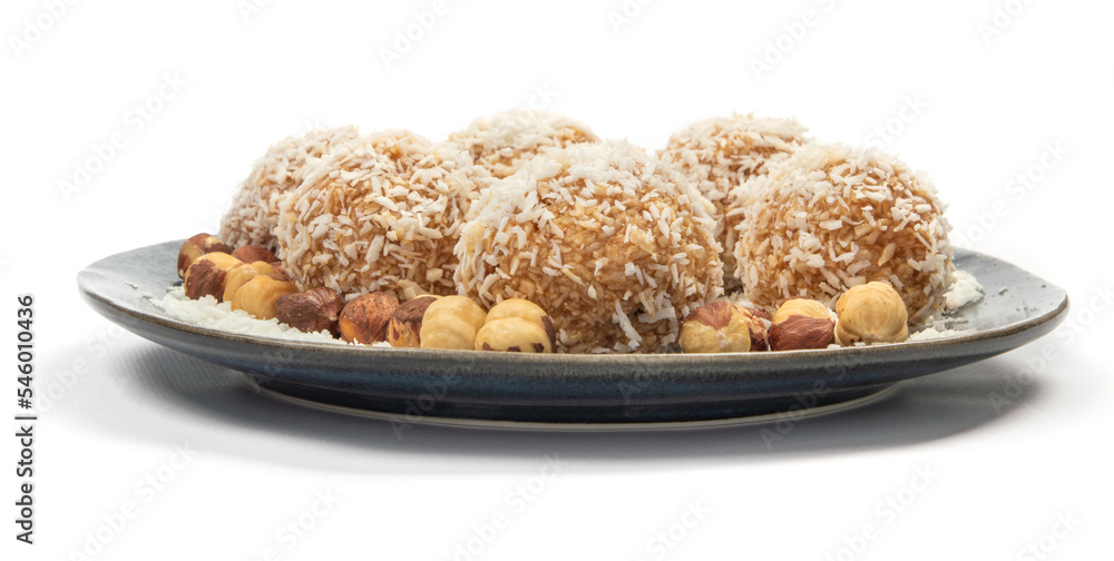 homemade coconut candies with almonds inside, sprinkled with coconut chips, lying on a round plate of dark blue color, decorated with hazelnuts isolate homemade coconut candies with almonds inside, sprinkled with coconut chips, lying on a round plate of dark blue color, decorated with hazelnuts isolate