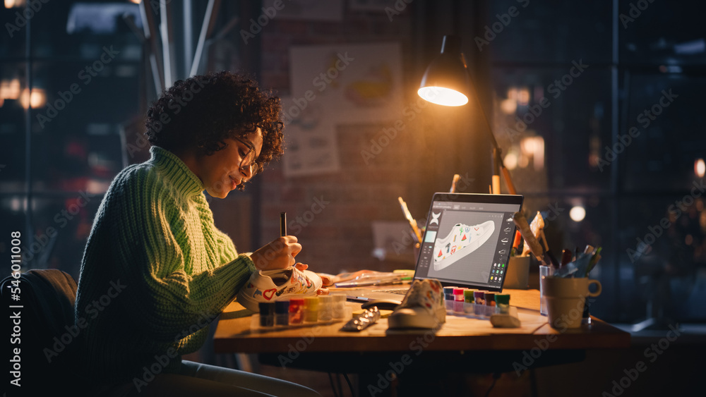 Creating Trendy Design. Black Woman Feels Inspired While Drawing in the Evening. Female Designer Puts Patterns on Shoe Comparing with 3D Model on the Laptop Computer Screen. Creating Trendy Design. Black Woman Feels Inspired While Drawing in the Evening. Female Designer Puts Patterns on Shoe Comparing with 3D Model on the Laptop Computer Screen.