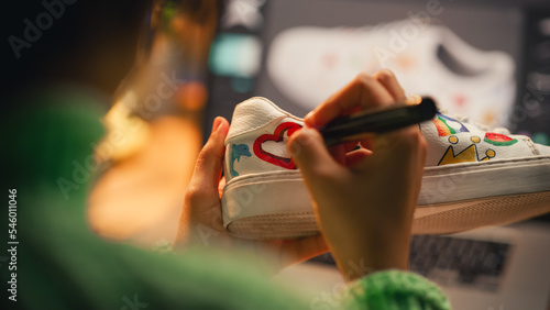 Close Up Over the Shoulder View of Black Female Artist Applying Colourful Brave Design on Sneakers while Spending Time at Home. Girl Customising Footwear in the Evening. Drawing on Shoes Concept. photo