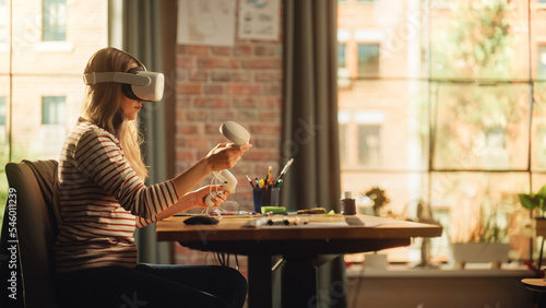 Blonde Woman Wearing 3D VR Headset And Using Modern Controllers in Loft Apartment Living Room. Female Designer Working in Futuristic Application. New Technologies and Augmented Reality Concept.