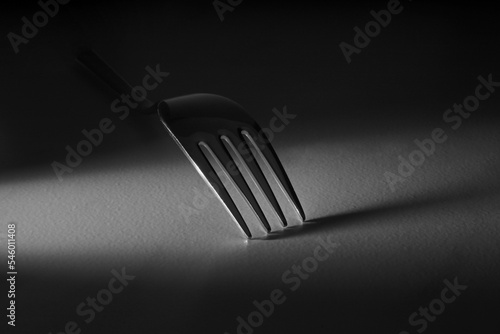 a metal fork with shadows on dark black and white background