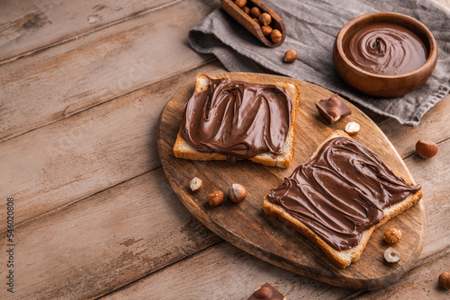 Obraz na plátně Board of bread with chocolate paste and hazelnuts on wooden background