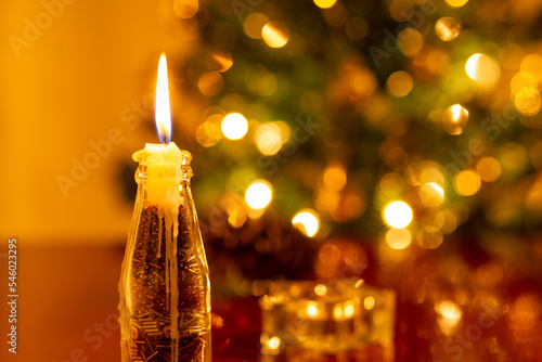 Decoração de Natal. Uma vela acesa em primeiro plano e uma árvore de Natal desfocada ao fundo.