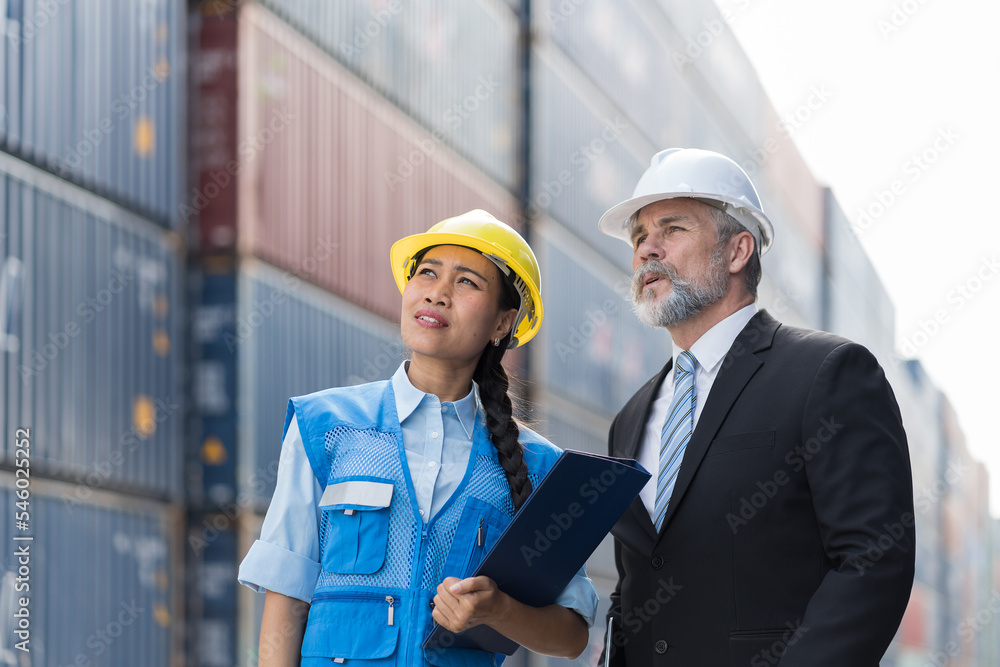 Senior male supervisor and asian female industrial engineer discussing, working at container terminal. Inspector or supervisor in container terminal. Ship, port, container and cargo industry
