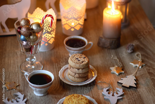 Two types of cookies, cups pf tea or coffee, various Christmas decorations and lit candles. Cozy Christmas atmosphere at home. Selective focus.