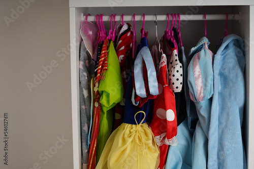 A background of Female childish wardrobe apparel hung comfortable vertical storage. Kids' girl clothes and Halloween costumes neatly hanging in a cupboard.