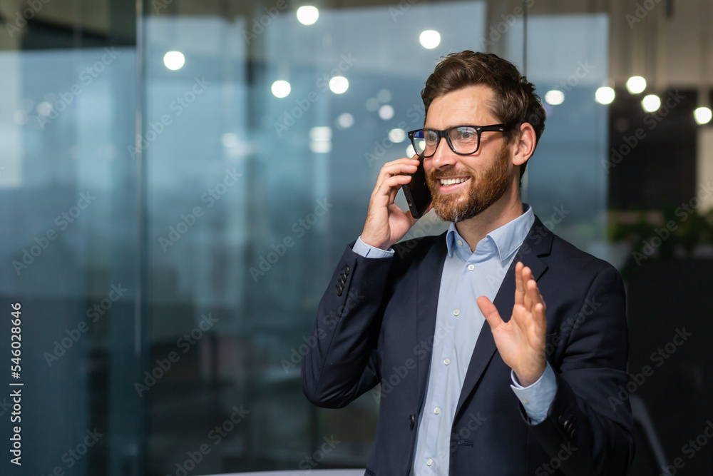 © Liubomir - Mature businessman in a business suit talking on the phone, the manager is satisfied with the result of the achievement and work talks about the positive result, the man is at work inside the office. © Liubomir - Mature businessman in a business suit talking on the phone, the manager is satisfied with the result of the achievement and work talks about the positive result, the man is at work inside the office.