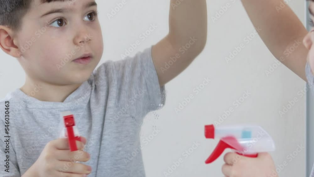 housekeeping and cleaning.cute kid little boy clean mirror glass with spray and micro fiber pink cloth.smiling child helping mother mom to do chores having fun work like playing.spray on mirror flows housekeeping and cleaning.cute kid little boy clean mirror glass with spray and micro fiber pink cloth.smiling child helping mother mom to do chores having fun work like playing.spray on mirror flows