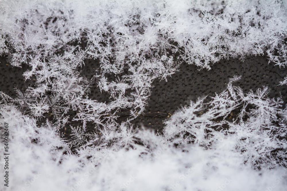Macro image showing thousands of snowflake specimens. Snow covering a dark grey/black background with a window on middle right side of frame. 