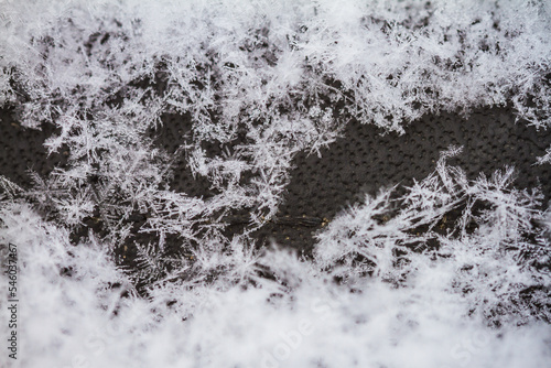Macro image showing thousands of snowflake specimens. Snow covering a dark grey/black background with a window on middle right side of frame.  © Mat