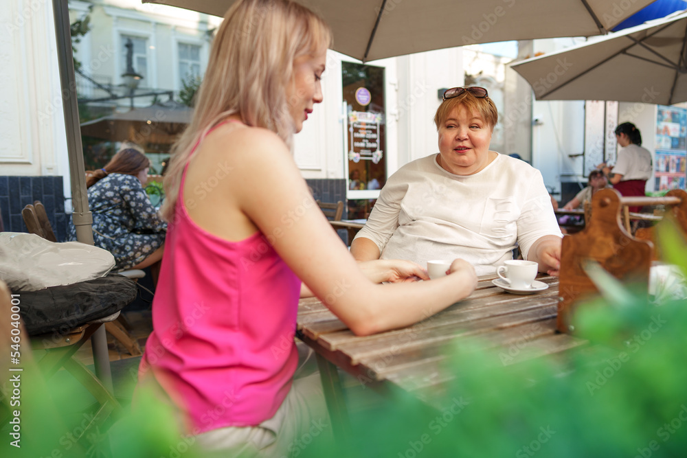 Young daughter and her mother in wheelchair sitting at the table in cafe with drinks and having fun